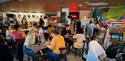 Photo de l'intérieur du café : tables éparses, dense de monde, murs colorés peints, plafond en bois