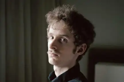 Une photographie du visage de Jérôme Blin qui regarde l'objectif dans un décor de chambre.