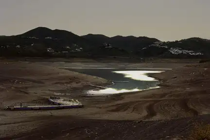 Une photographie prise dans le sud de l'Espagne d'une étendue d'eau. Des montagnes se détachent du fond de l'image et le soleil au crépuscule se reflète dans l'eau.