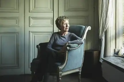 Une photographie de Michelle Perrot, assise dans un fauteuil élégant. Elle regarde dehors par la fenêtre.