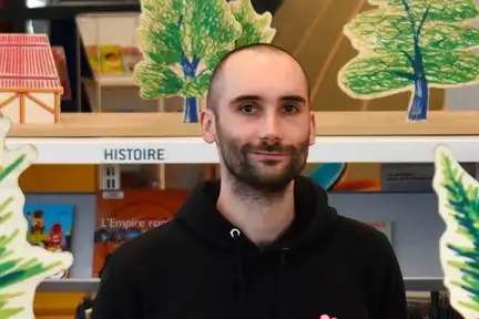 Une photographie de Valérian Henry qui sourit devant ses dessins réalisés pour l'installation participative L'Ouest fantastique à la Bibliothèque des Champs Libres.