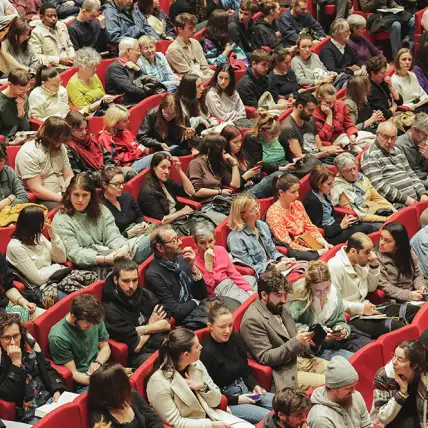 Dans une assemblée de fauteuils rouges, des dizaines de jeunes sont assis.