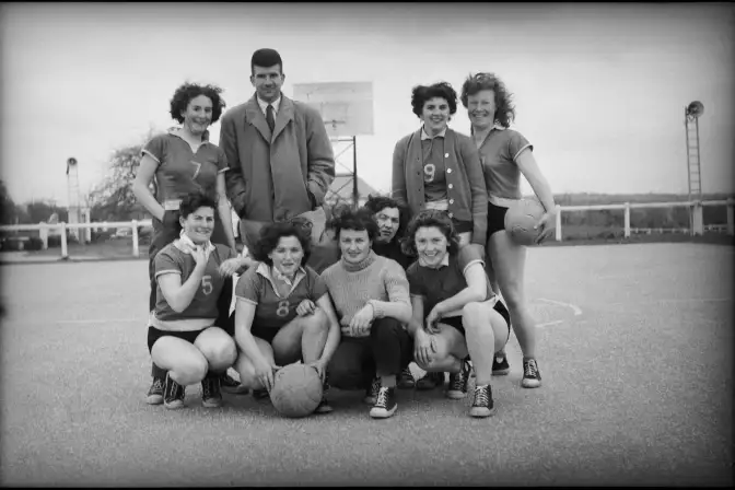 huit basketeuses souriantes accompagnées de leur dirigeant tiennent la pause sur un terrain de basket en extérieur