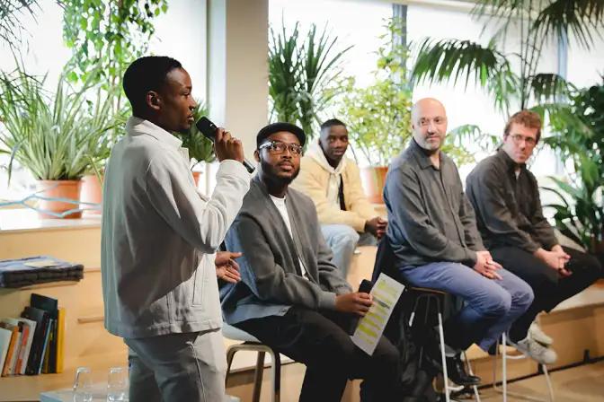 Sur cette photo, cinq hommes sont en train de parler à l'occasion de l'événement Nos Futurs 2024. Quatre d'entre eux sont assis et écoutent le cinquième parler au micro sur un sujet divers.