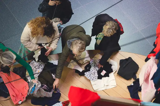 Cette photographie prise de haut nous montre des femmes en train de choisir des vêtements à l'occasion de l'événement Nos Futurs de 2024. On peut les apercevoir chercher des vêtements sur le terrain de jeux dans le hall.