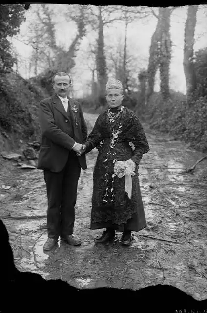 Une photographie en noir et blanc d'un couple se tenant la main en fixant l'objectif en pleine nature. Les deux personnes sont élégamment habillées.