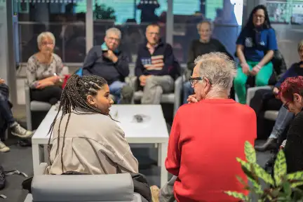 Un groupe de personnes assises en cercle. Au premier plan une jeune femme et un homme échangent tandis que les autres personnes écoutent