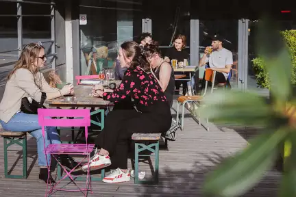 Photo de la terrasse du Café des Champs Libres : sol en lattes de bois, tables en métal, soleil, grand plans végétaux.