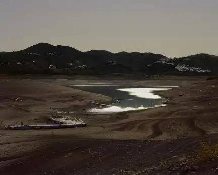 Une photographie prise dans le sud de l'Espagne d'une étendue d'eau. Des montagnes se détachent du fond de l'image et le soleil au crépuscule se reflète dans l'eau.