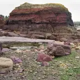 Photographie de l'Ande de Bréhec en Côtes d'armor. Une roche rouge se détache d'une plage de galet.