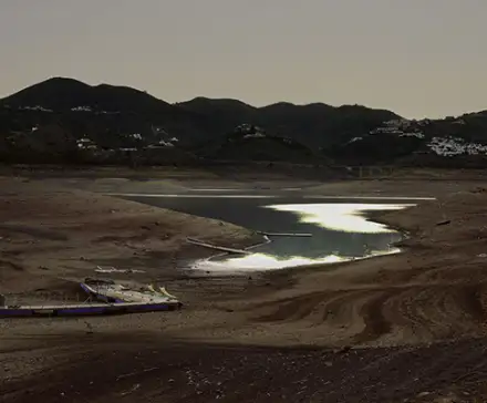 Une photographie prise dans le sud de l'Espagne d'une étendue d'eau. Des montagnes se détachent du fond de l'image et le soleil au crépuscule se reflète dans l'eau.