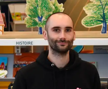 Une photographie de Valérian Henry qui sourit devant ses dessins réalisés pour l'installation participative L'Ouest fantastique à la Bibliothèque des Champs Libres.